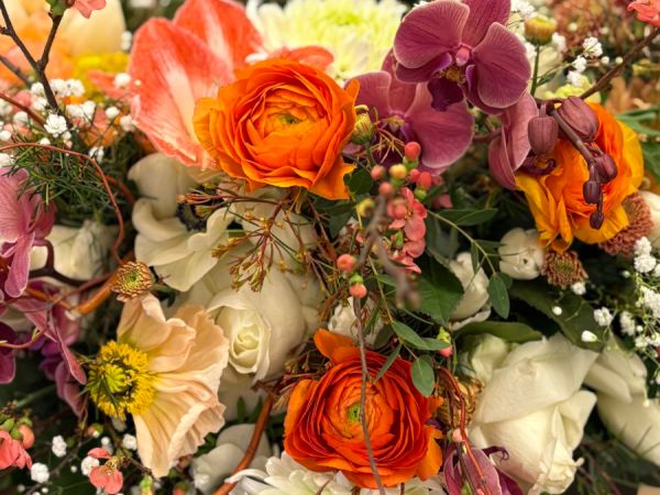 Außenansicht eines Blumenladens mit Schaufenster voller Pflanzen, Blüten, Dekorationen und einer großen geflochtenen Figur.